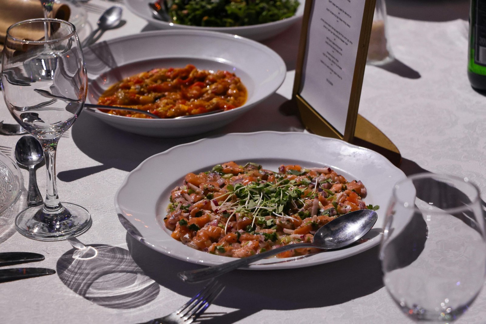 A sophisticated dinner setup featuring a dish of salmon tartare garnished with greens.