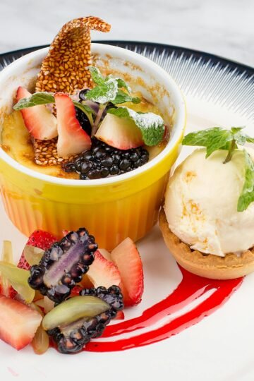Indulge in a gourmet crème brûlée topped with blackberries and strawberries, paired with vanilla ice cream.