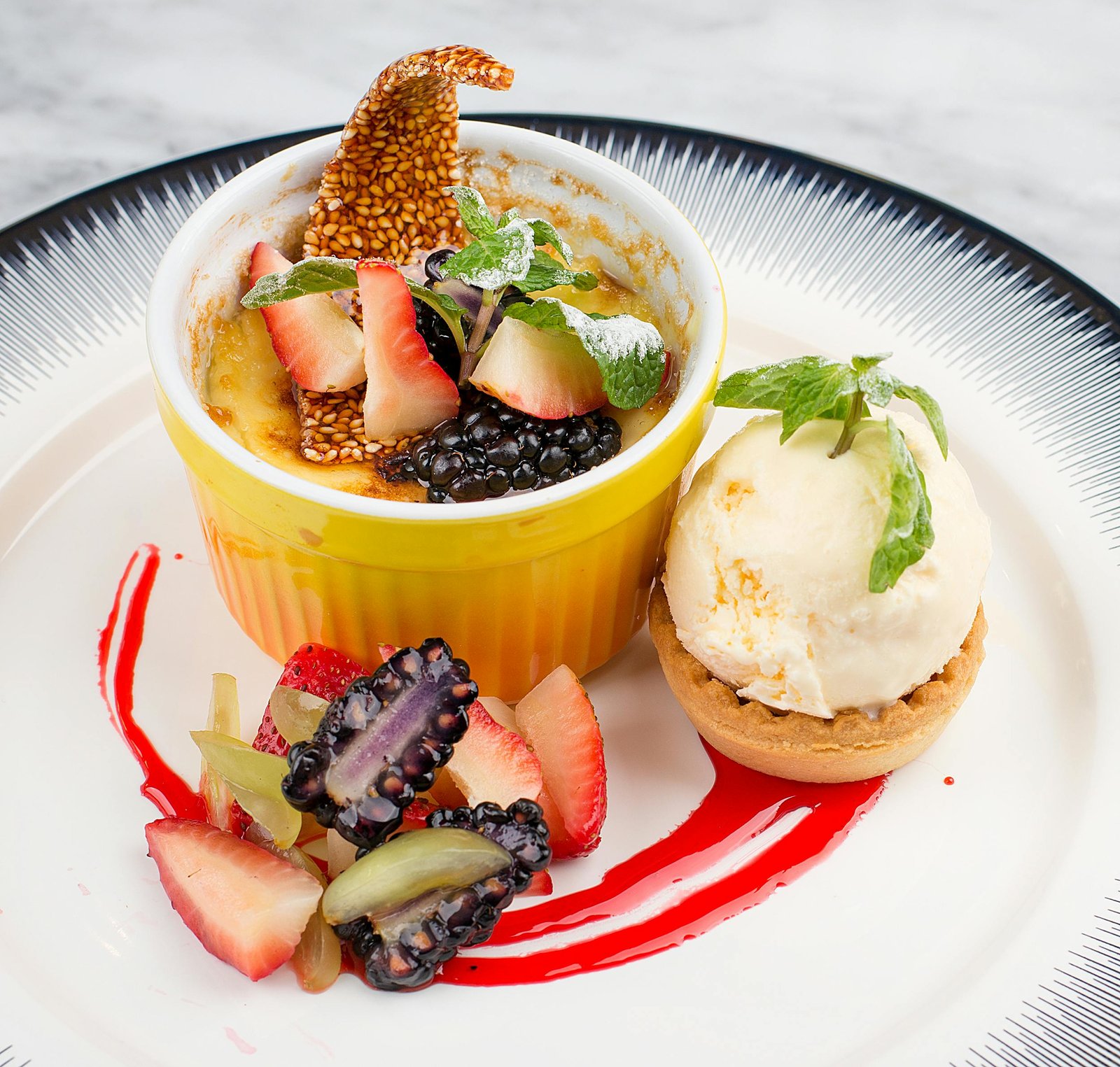 Indulge in a gourmet crème brûlée topped with blackberries and strawberries, paired with vanilla ice cream.